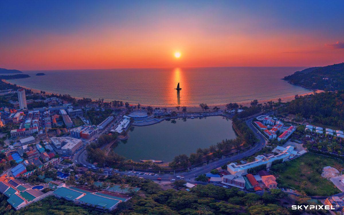 A vivid sunset illuminates a lone sailboat at Karon beach in Phuket, Thailand, creating a gorgeous aerial shot.